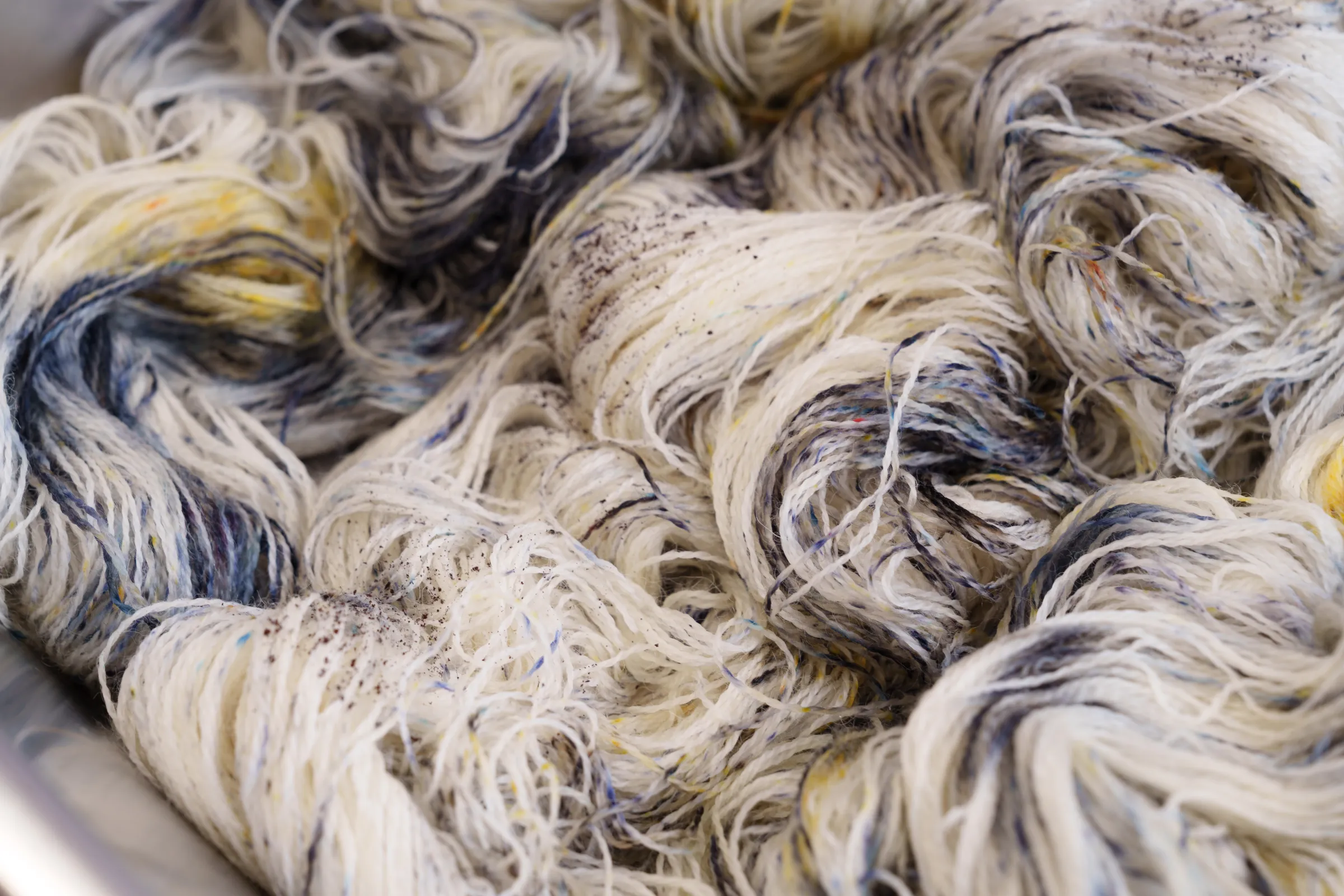 Undyed wool skeins scattered with dye speckles in a steel tray
