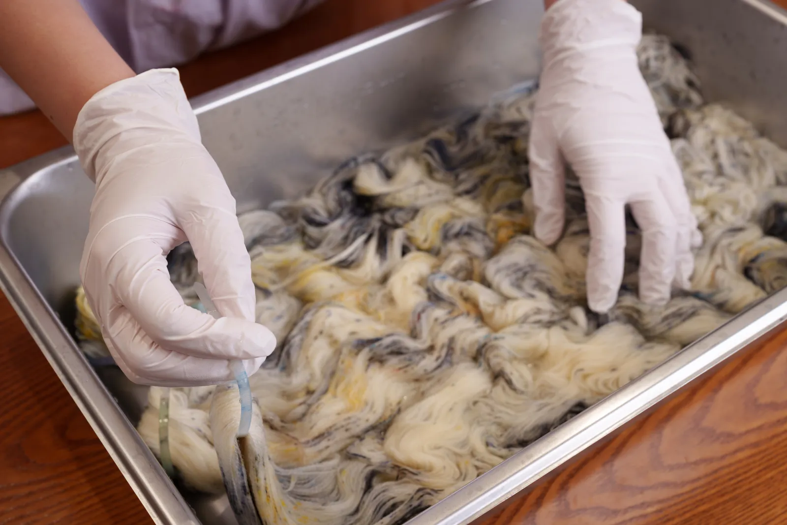 Gloved hands working speckled skeins in a steel dye tray